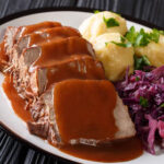 Delicious traditional German dinner Sauerbraten - slowly stewed marinated beef with gravy with potato dumplings and red cabbage close-up on a plate. horizontal